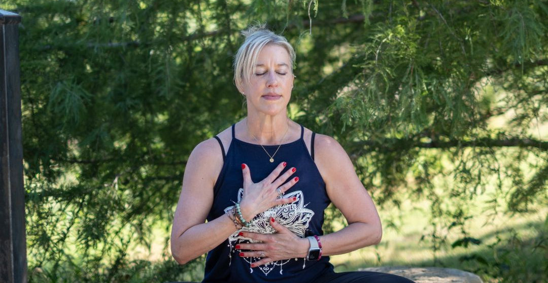 Woman meditating outdoors on a stone ledge with trees in the background